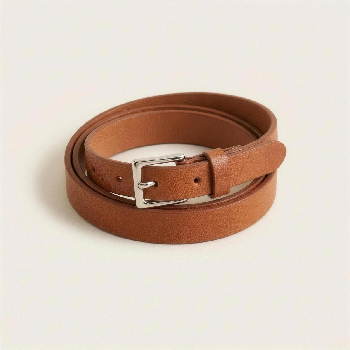 Slim tan leather belt with a polished silver pin buckle, coiled