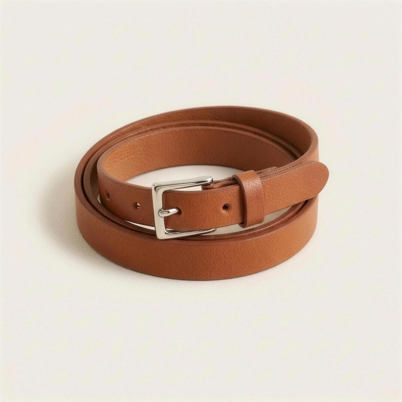 Slim tan leather belt with a polished silver pin buckle, coiled